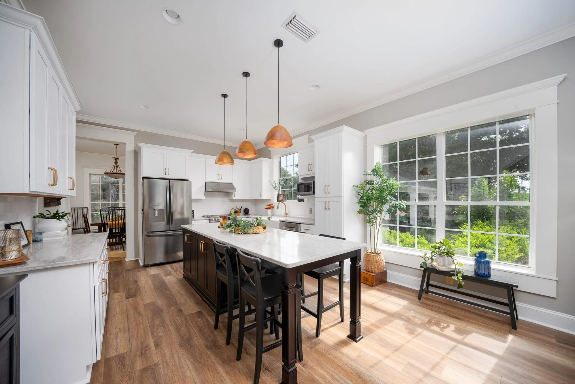 A remodeled kitchen with a marble island, copper pendant lights and wide plank floors