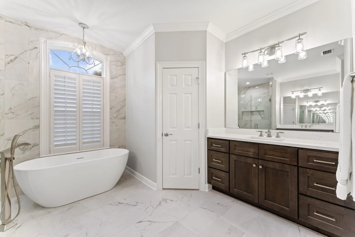 A remodeled bathroom with a freestanding tub, marble tile and a dark wood vanity