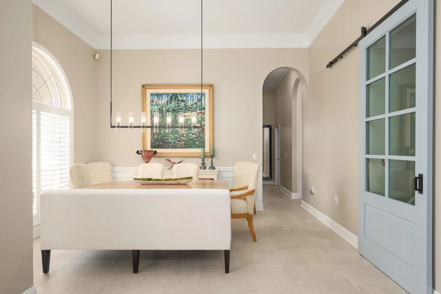 A dining area with large format tile flooring, an arched doorway and a sliding barn door