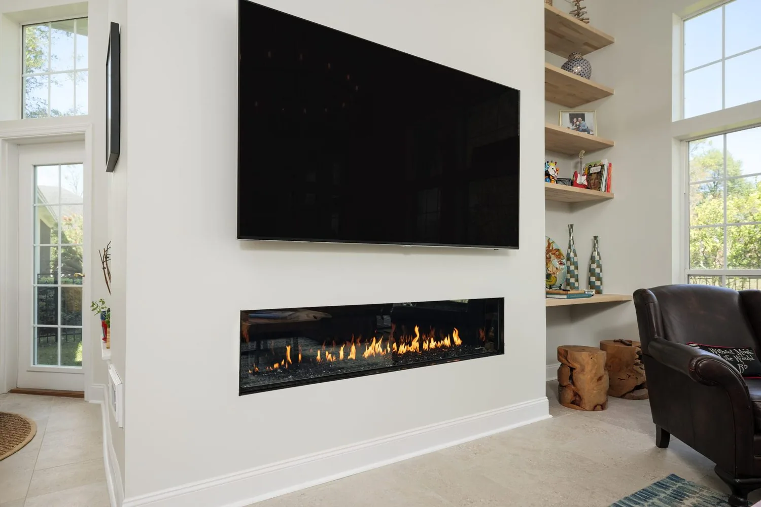 A remodeled living room with a linear fireplace, built-in shelving and tall windows