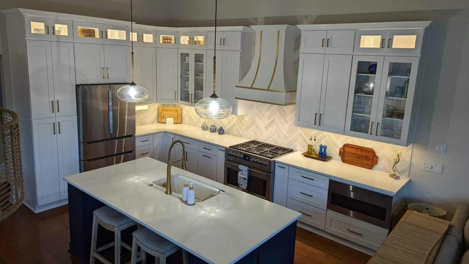 A remodeled kitchen with a navy island, brass faucet and herringbone backsplash